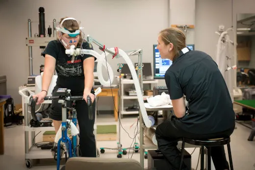 Person riding a bike while wearing testing equipment with a researcher besides them