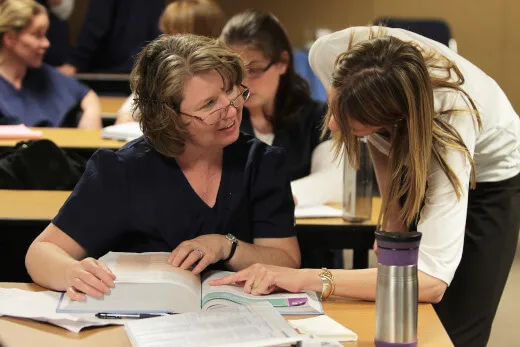 Teacher helping a student by pointing to something in a textbook